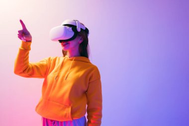 Sarı kapüşonlu ve VR kulaklık takan beyaz güzel bir kadın arka planda kırmızı ve mavi bir ışık, fütüristik teknoloji ve giyilebilir cihaz konseptiyle sanal gerçeklik yaşıyor.
