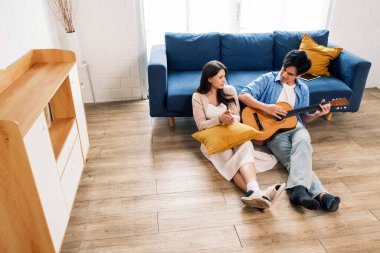 Çekici yeni evli erkek ve kadın yerde oturup yeni evdeki oturma odasında gitar çalmanın ve şarkı söylemenin keyfini çıkarıyorlar. Bir aile, yeni bir eve taşındıktan sonra birlikte kaliteli zaman geçirir..