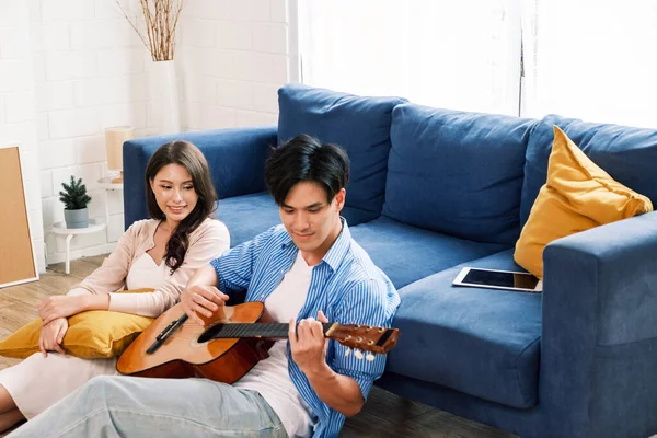 Attractive new marriage man and woman sit on the floor enjoy singing and playing guitar in the living room at the new home. A family spends quality time together after moving into a new home.