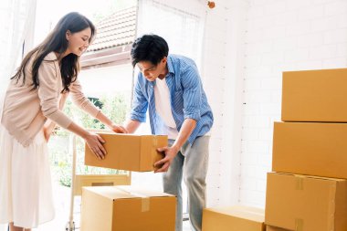 Asyalı genç mutlu evli çift yeni evlerine ya da gayrimenkullerine taşınıyor. Çekici romantik bir erkek ve kadın, içinde mutluluk ve sevgi olan kutular taşır. Aile taşınma konsepti.
