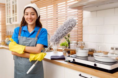 Evde çalışan iki Asyalı temizlikçi kadın işçinin portresi. Temizlikçi kızlar, toz bezi, sisli sprey ve bez parçalarını tutun. Ev işlerini bitirdikten sonra kameraya bakın..