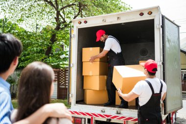 Üniformalı Asyalı ve Kafkasyalı işçiler kamyondan karton kutuları boşaltıyorlar. Teslimatçılar kutuları boşaltıyor ve iş arkadaşlarıyla kontrol ediyorlar. Profesyonel dağıtım ve taşıma hizmeti.