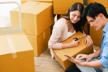 Mutlu Asyalı çift yeni bir eve taşınıyor kadın eski evdeki karton kutuları açarken erkek dijital tabletle online alışveriş yapıyor. Aile Taşımacılığı, Ev Taşımacılığı Konsepti.