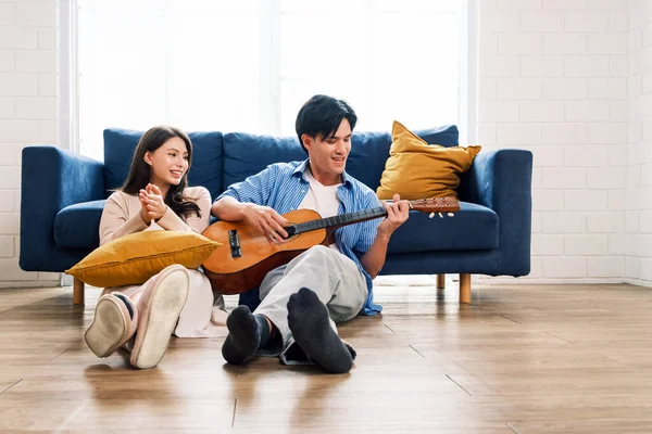 Attractive new marriage man and woman sit on the floor enjoy singing and playing guitar in the living room at the new home. A family spends quality time together after moving into a new home.