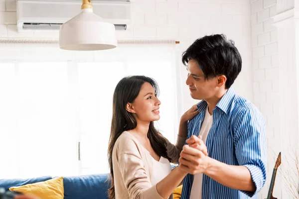 Attractive young Asian couples enjoy having a lovely romantic dance in the living room of the apartment. A family spends quality time together after moving into a new home. Image with copy space.