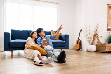 Çekici yeni evli erkek ve kadın oturma odasında yerde birlikte oturup yeni evdeki fotokopi alanını işaret ediyorlar. Bir aile, yeni bir eve taşındıktan sonra birlikte kaliteli zaman geçirir..