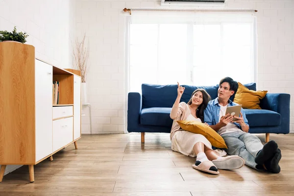 Attractive new marriage man and woman sit on the floor together in the living room and point on copy space at the new home. A family spends quality time together after moving into a new home.