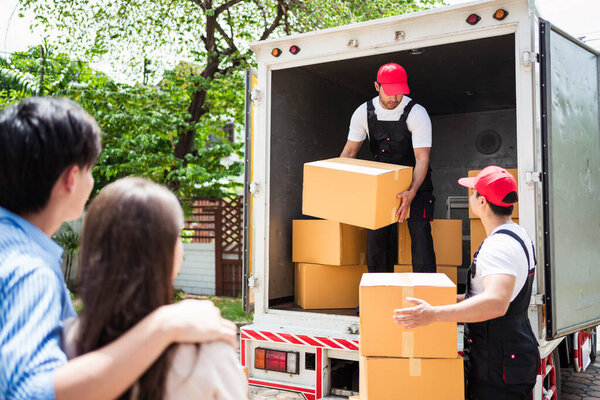 Asian and Caucasian workers in uniform unloading cardboard boxes from the truck. Delivery men unloading boxes and check the checklist with their coworkers. Professional delivery and moving service.