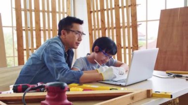 Neşeli Asyalı marangozluk babası oğluna atölyede dizüstü bilgisayardaki inşaat aletlerini anlatıyor ve öğretiyor. İnşaat işi ve tamirat. Marangozluk ve aile kavramı.