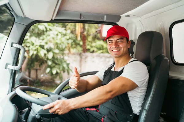 Happy professional truck driver with his assistant wearing a red cap thumb up, smiling, looking at the camera from a truck window before delivering parcel. A truck driver and delivery service concept.