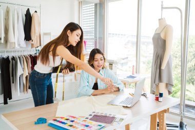 İki Asyalı moda tasarımcısı veya terzisi yeni koleksiyonun tasarımını dizüstü bilgisayarında kumaş ve çizim örnekleriyle tartıştılar. Stüdyoda birlikte çalışıyoruz..