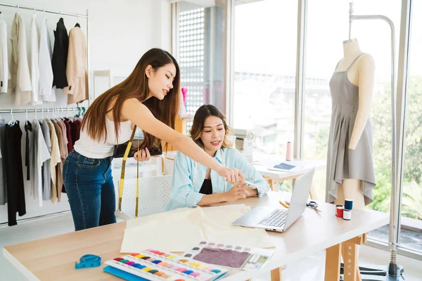 İki Asyalı moda tasarımcısı veya terzisi yeni koleksiyonun tasarımını dizüstü bilgisayarında kumaş ve çizim örnekleriyle tartıştılar. Stüdyoda birlikte çalışıyoruz..