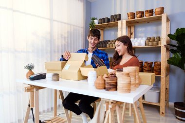 Beyaz erkek ve Asyalı kadın vazo ürünleri evde canlı yayında satıyorlar. Müşterilere gönderilmek üzere vazo paketleme işlemi. Uzak satın alma, çevrimiçi alışveriş kavramı.