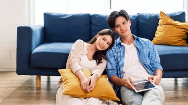 Elinde tablet olan çekici evli bir adam ve bir kadın oturma odasında yerde oturup yeni evdeki kameraya bakıyorlar. Bir aile taşındıktan sonra birlikte kaliteli zaman geçirir..