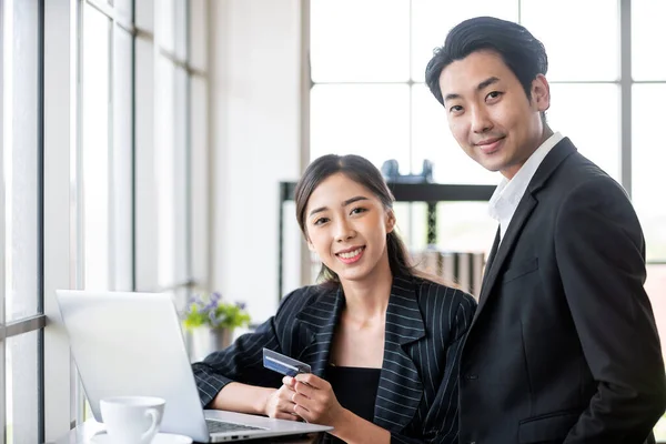 Two Asian business people use a credit card for online payments. Business people shop online, e-commerce, internet banking and spend money with security and confidence.