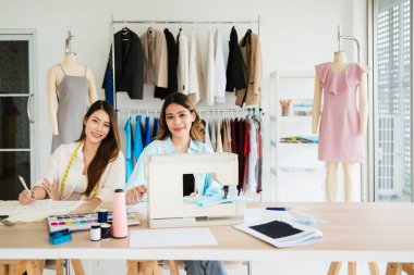 İki Asyalı moda tasarımcısı ya da terzisi, tablet üzerindeki kumaş ve çizim örnekleriyle yeni koleksiyonun tasarımını tartıştılar. Stüdyoda birlikte çalışıyoruz..