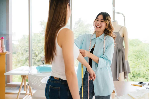 Asian woman tailor measures customers\' bodies to make new clothes. Attractive female fashion designer dressmaker working and designing new fashion collections for customers in atelier tailor workshop.