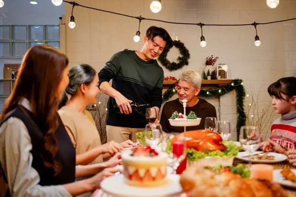 Happy and Cheerful group of extended Asian family talking and smiling during Christmas dinner at home. Celebration holiday togetherness. Family gatherings and reunions. Focus on young Asian father.