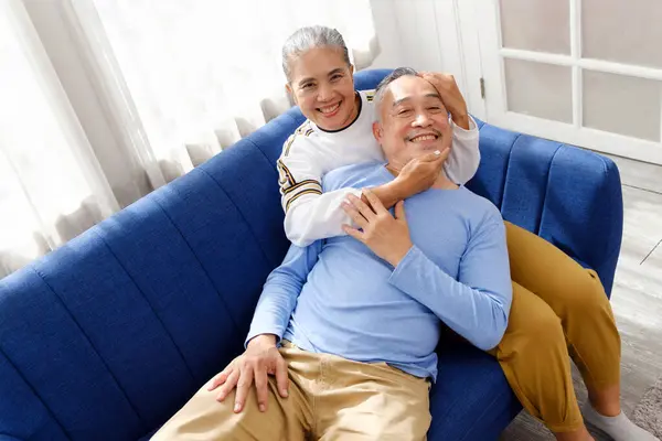 Portrait of happy Asian senior couple living together, hug, touching and embracing with a smile on the sofa in the living room. Retirement living together at home.