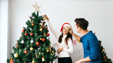 Mutlu genç çift evdeki oturma odasındaki Noel ağacında çeşitli takılar süslerken eğleniyor. Noel tatilinin tadını çıkarıyor ve kutluyoruz.