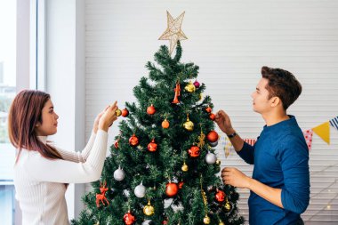Mutlu genç çift evdeki oturma odasındaki Noel ağacında çeşitli takılar süslerken eğleniyor. Noel tatilinin tadını çıkarıyor ve kutluyoruz.
