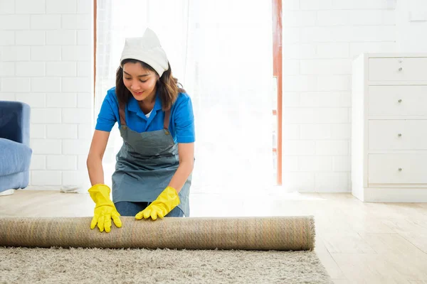 Two Asian young professional cleaning service women worker team working in the house. Girl housekeeper rolled keeping the carpet before cleaning wooden floor. Cleaning service. Photo with copy space