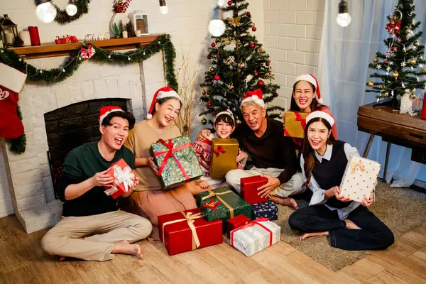 快乐快乐的亚洲家庭聚在一起 头戴圣诞礼帽 谈笑风生 交换礼物 祖父母 孙子孙女 坐在壁炉边 装饰着圣诞树 免版税图库图片