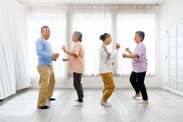Active Asian senior group mix with man and woman exercise by dancing together at home with relaxing, smiling and laughing. Indoor activity for mature seniors and retirement people. Focus on senior man