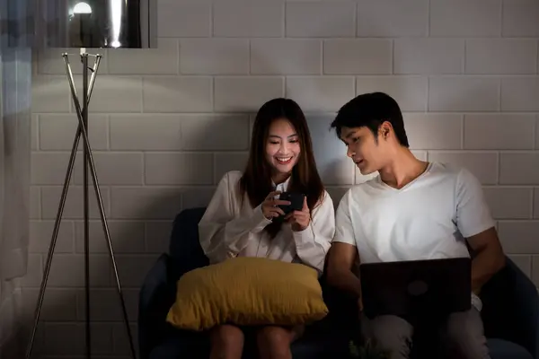 Asian couple working late from home with a laptop in the dark bedroom. Husband and wife discuss and brainstorm together at night before the business work deadline. Night working, Working late concept.