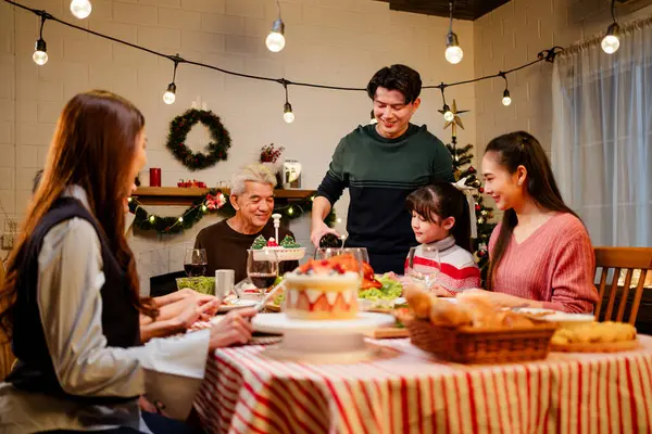 Happy and Cheerful group of extended Asian family talking and smiling during Christmas dinner at home. Celebration holiday togetherness. Family gatherings and reunions. Focus on young Asian father.