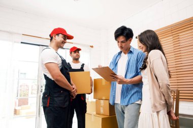 Birkaç kişi, üniformalı Asyalı ve Kafkasyalı işçilerin karton kutuları boşalttıkları listeyi imzaladı. Teslimatçılar çiftler için kutuları boşaltıyor. Profesyonel dağıtım ve taşıma hizmeti.