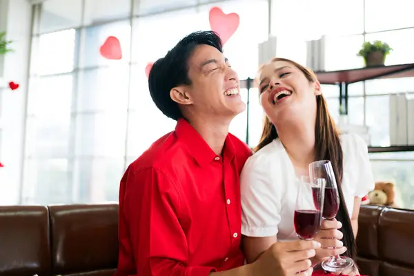 A young happy Asian couple talking and laughing while drinking red wine together on her anniversary date at home. Asian woman enjoy drinking with her boyfriend. Valentine\'s Day celebration concept.