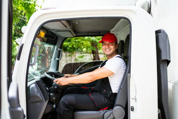 Happy professional truck driver with his assistant wearing a red cap, smiling, looking at the camera from a truck window before delivering parcel. A truck driver and delivery service concept.