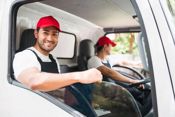 Happy professional truck driver with his assistant wearing a red cap, smiling and looking at the camera from a truck window before delivering parcel. A truck driver and delivery service concept.
