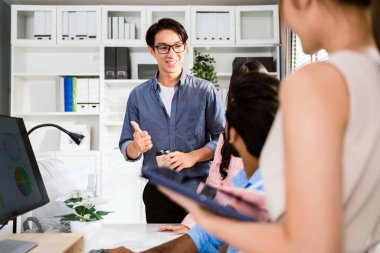 Asyalı genç iş adamlarından oluşan neşeli ve kendinden emin bir grup sıradan bir gülümseme ve bir ekip için baş parmak kaldırarak toplantı sırasında tartışıyorlar. Bir toplantıda iş adamlarının çeşitliliği.