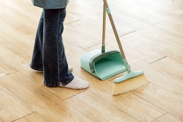 Crop image of a young professional cleaning service women worker working in the house. Girls housekeeper sweeps broomsticks on the wooden floor and cleaning under the sofa. Cleaner and chore concept