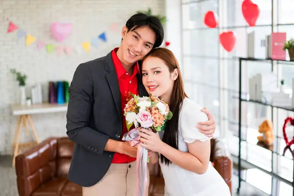 A young Asian man surprised his girlfriend by giving her a rose and flower bouquet for her anniversary date at home. Asian woman enjoy receiving bouquet from her boyfriend. Valentine\'s Day celebration