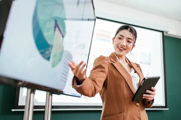 Portrait of a smart Asian young entrepreneur businesswoman using her digital tablet while standing in the office. A businessman wearing a blazer while using a tablet for meeting with a smile.