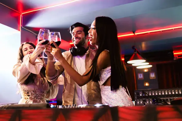 Group of energetic women dancing friends with DJ enjoying night party. Young women dance and hold a wine glass in nightclub. Nightlife, disco dance and girl's night party concept. Fun music festival
