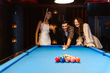 Genç çeşitlilikteki insanlar gülümseme, keyif ve eğlenceyle bilardo oynuyor. Gençler gece kulübündeki bilardo salonunda vakit geçiriyorlar. Erkekler, kadın arkadaşlar bilardo oynuyor. Gece hayatı konsepti