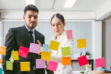 Bir grup başarılı Asyalı iş adamı takım çalışması. Yeni fikirler için cam duvarda yapışkan kağıt notlarla beyin fırtınası toplantısı. Bir teknoloji şirketinde iş için çevik metodoloji kullanmak.