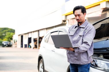 Japon bir otomobil tamircisi tamir ve onarım için araba motor parçalarını teşhis etmek ve kontrol etmek için bir bilgisayar dizüstü bilgisayar kullanır. Asyalı araba tamirhanesi servis merkezi. Açık hava profesyonel servisi.