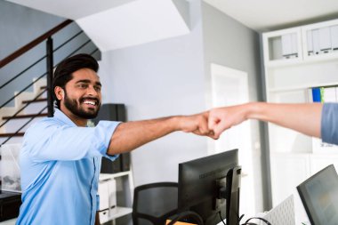 Neşeli Hintli iş ortakları takım çalışmasının sembolü olarak gülümseyerek yumruk tokuşturuyorlar. Ofiste çeşitlilik konusunda çok ırklı iş arkadaşları var. İşbirliği kavramı