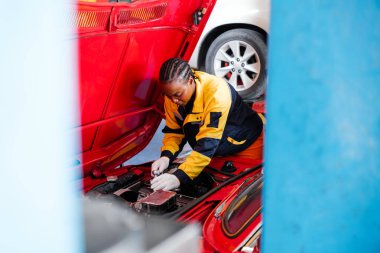 Çeşitlilik mekanik ekip çalışması, sarı ve mavi üniformalı Afrikalı bir kadın açık radyatör kaputu müşteri otomobili motorunu inceliyor. Otomobil tamirat servisi. Araç bakımı. Profesyonel hizmet.