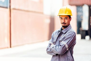 Sarı şapkalı çekici Japon sanayi mühendisi, arka planda bulanık bir konteynır deposu olan güvenlik üniforması. Lojistik merkezinde çalışıyorum. Müfettiş, konteyner terminalinde denetleyici.