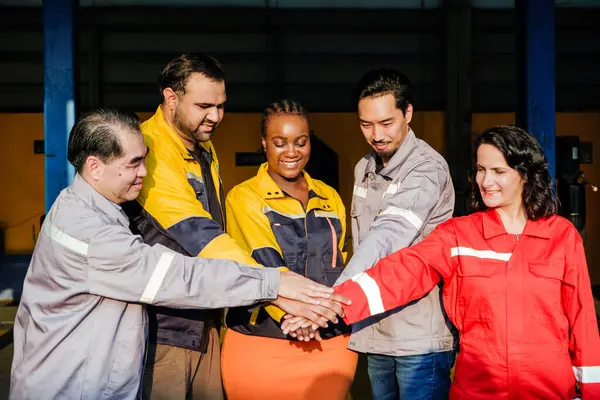 Group of diversity male and female car service labor stand and join hands together in front of the garage. Everyone wear safety uniform and working in auto repair shop. Blue-Collar Labor Day concept.