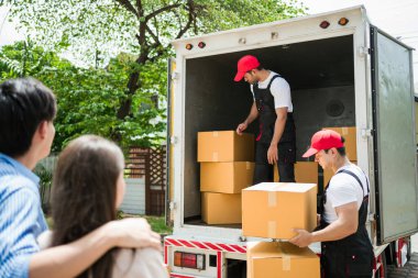 Üniformalı Asyalı ve Kafkasyalı işçiler kamyondan karton kutuları boşaltıyorlar. Teslimatçılar kutuları boşaltıyor ve iş arkadaşlarıyla kontrol ediyorlar. Profesyonel dağıtım ve taşıma hizmeti.