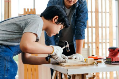 Mutlu Asyalı baba ve oğlu marangoz ve marangoz olarak çalışıyor. Baba oğluna tahta tahtaya çivi çakmayı birlikte dikkatlice öğretiyor. Marangozluk atölyesinde çalışıyor..