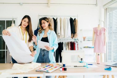 Asyalı kadın moda tasarımcısı ya da terzi kesik kağıt kumaş kalıplarını hazırlamaya yardım ediyor. Atölye terzi atölyesinde çalışan ve yeni moda koleksiyonları tasarlayan bir terzi..