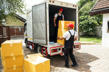 Üniformalı Asyalı ve Kafkasyalı işçiler kamyondan karton kutuları boşaltıyorlar. Teslimatçılar kutuları boşaltıyor ve iş arkadaşlarıyla kontrol ediyorlar. Profesyonel dağıtım ve taşıma hizmeti.